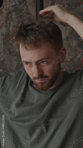 Man touching hair under dryer, quiet self care moment with soft light, introspective expression and slow deliberate movements