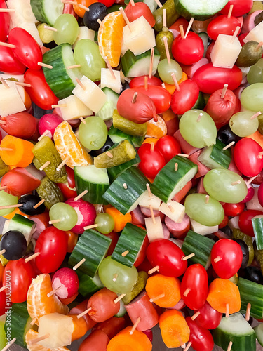 Top view of assorted canapes with vegetables, fruits, cheese and sausages on wooden skewers, party food and appetizer