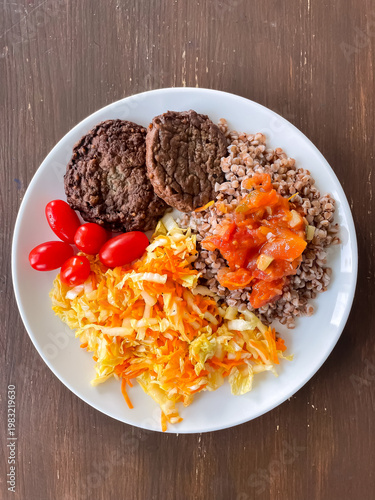 Top view of plate with balanced meal of buckwheat in tomato sauce, cutlets, cabbage salad and cherry tomatoes, healthy eating and nutrition
