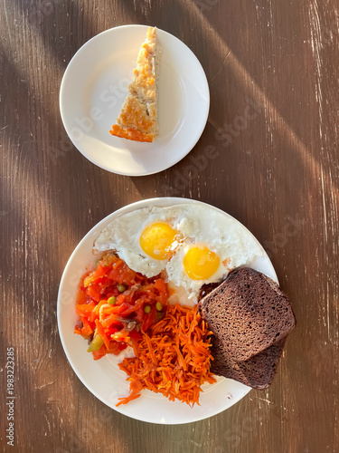 Top view of plate with balanced meal of fried eggs, rye bread, stewed vegetables, carrot salad and cottage cheese casserole, healthy eating and nutrition
