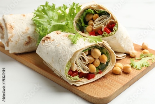 Pieces of tasty wrap with chickpeas and vegetables on white table, closeup