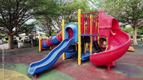 A happy little Indonesian girl playing on a slide in an outdoor playground. Slow motion.
