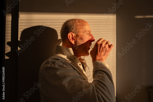 Stockholm, Sweden A man drinks coffee in the early morning in the shadow of window shades.