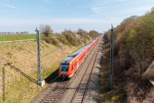 Fotografie Red passenger train traveling on a railway track with motion blur, high angle vi