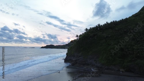 Aerial view of tropical coastline with waves and hills at sunset