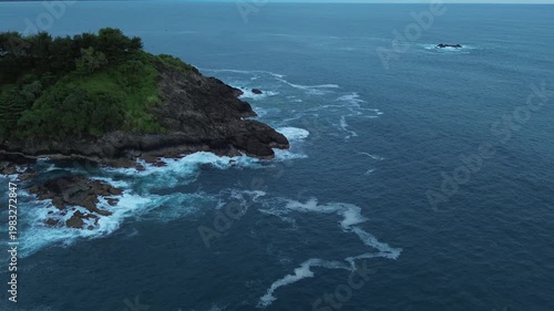 Aerial view of rocky coastline with crashing waves, showcasing the dynamic interaction between ocean water and rugged shore, highlighting the natural beauty of the coastal landscape