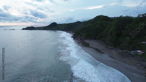 Aerial view of tropical coastline with waves and hills at sunset