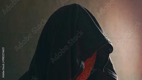 Schilderij op canvas A hooded male figure is seen in profile with a striking red glow illuminating his textured mask, creating a highly intense and dangerous mood