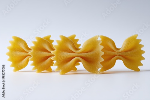 Three golden bow-tie shaped pasta pieces lined up on a plain white surface