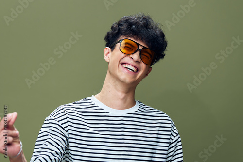 Photography Young man laughing joyfully wearing sunglasses and striped shirt against soft green background, capturing happiness and casual style in modern portrait photography