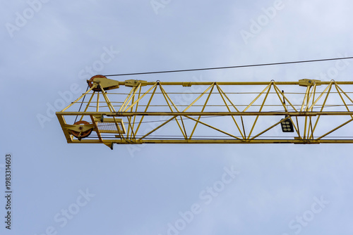 Fotografie Low angle view of yellow tower crane jib against blue sky, industrial heavy lift