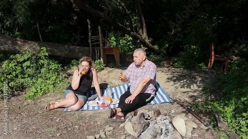 A man and a woman are preparing a barbecue on an open fire near the river.