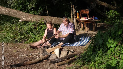 A man and a woman are preparing a barbecue on an open fire near the river.