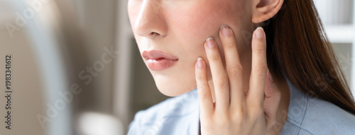 Fotografie Sensitive skin with cosmetology, Asian young woman looking at red spot on her face from cosmetic allergy in the mirror