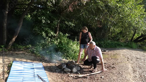 A man and a woman are preparing a barbecue on an open fire near the river.