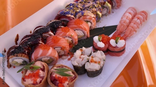 Close-up of fresh assorted sushi and rolls set in box with salmon, shrimp and caviar outdoors near yellow car. Perfect for food, Japanese cuisine and delivery themed projects