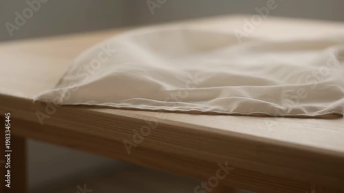 The video depicts a sequence showing a piece of fabric or cloth being placed, lightly folded, and then smoothed out on a wooden surface