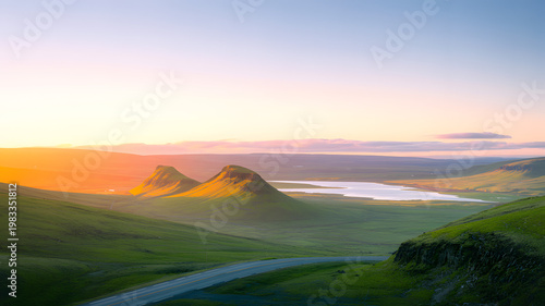 Rolling green hills bathed in golden sunrise light with a serene lake and distant mountains