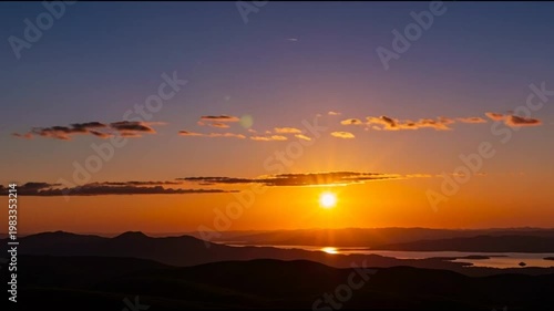 Vibrant sunset over mountains and water, dramatic sky with orange and purple hues.