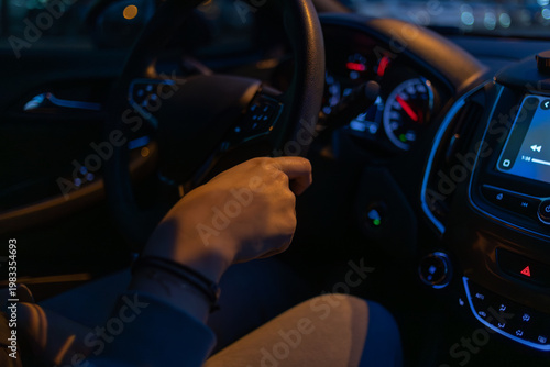 Night driving scene inside a modern car, driver hand on steering wheel with illuminated dashboard and multimedia screen, capturing urban motion, focus and advanced automotive technology