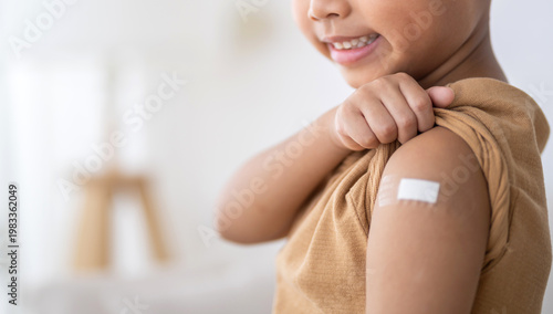 Close up asian child showing white bandage on arm after getting vaccination, Happy kid receiving rotavirus vaccine or flu shot, Child immunization, medical healthcare and pediatric clinic concept