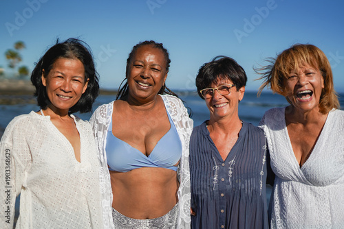 Happy senior multiracial women with different body hugging each other on the beach - Summer vacation, travel, holiday and diverse ethnic people concept