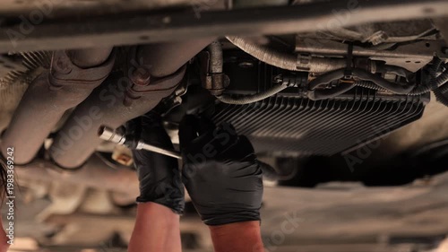Car mechanic fidgeting underneath a car on a suspension lift to try and remove a part. 