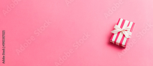 wrapped Christmas or other holiday handmade gift box in color paper with ribbon on colored background. Present box, decoration of gift on colored table, top view with copy space