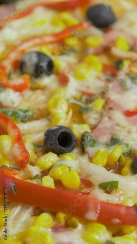 Newly baked pizza presents corn, pepper, onion, ham, olive, herb detail beneath soft cheese. Deep flavor dish at home kitchen