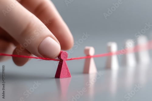Strategic Intervention: A hand meticulously manipulates a single game piece connected to others by a red thread, illustrating a strategic move within a complex system of interconnected components.