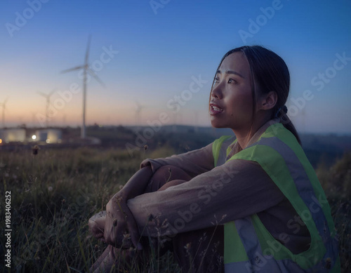 Woman wearing safety vest near wind turbines.