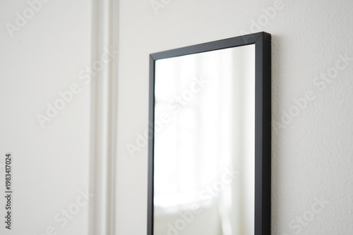 Minimalist black framed mirror hanging on a textured white wall with decorative molding