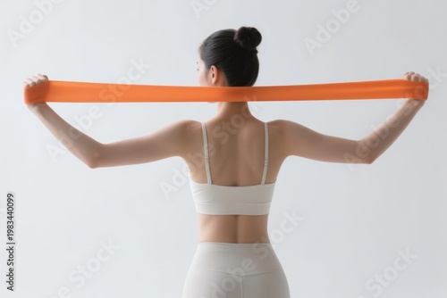 Woman performing resistance band exercise from behind, wearing white athletic wear against a neutral background