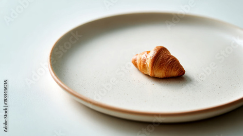 Single mini croissant on large plate in minimal composition emphasizing scale contrast. Conceptual mini food idea for modern branding advertising and creative food design visuals