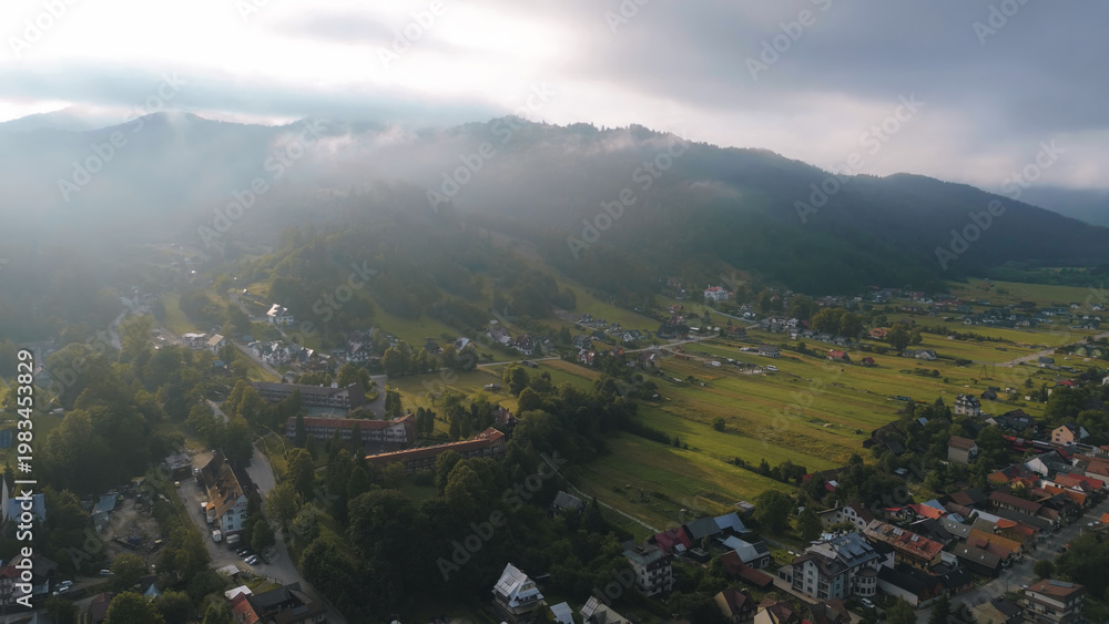 Fototapeta premium Mountain village houses nestling in a green valley, surrounded by dense forests and rolling hills, bathed in the warm, golden light of a morning sun