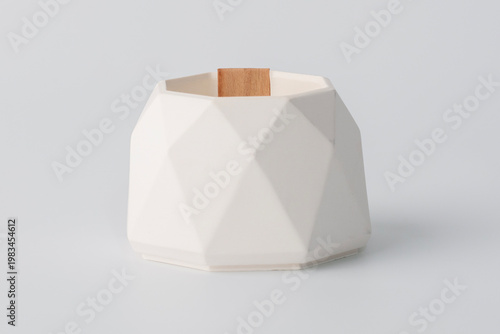 A candle with a white geometric pattern stands on a light background. This item is designed to decorate the interior and create a romantic atmosphere