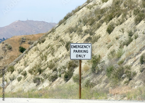 Emergency Parking Only sign on the side of the highway, desert hill landscape in the background.