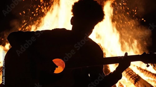 Young man playing guitar by campfire in evening darkness  