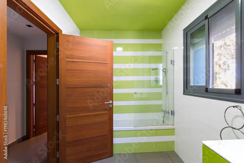 Modern bathroom featuring vivid striped tiles, wooden door, bathtub, and window