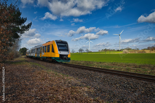 Modern Regional Train Passing Green Field with Wind Turbines - Sustainable Public Transportation Concept