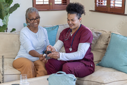 Fotografie Senior African American woman with nurse in maroon scrubs sitting on beige sofa