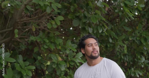 Adult man standing by shrub in yard hearing sound, turning scanning, smiling laughing in white T