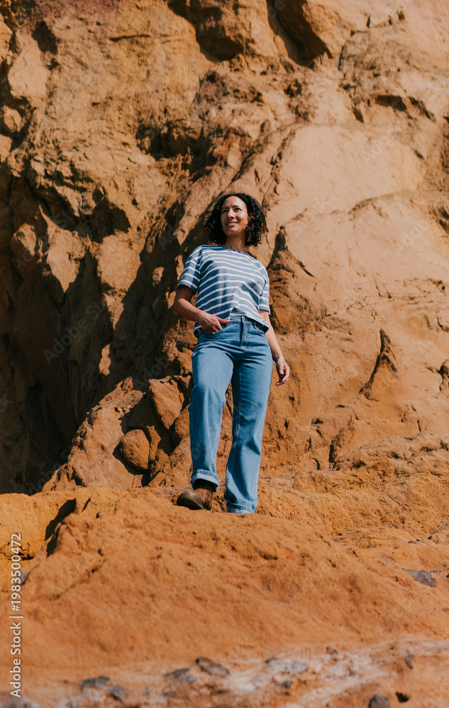 Naklejka premium Woman stands confidently on vibrant red rock cliffside