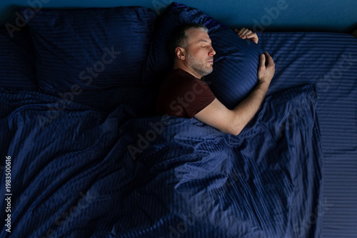 Obraz na plátně Top view of middle aged man sleeping on side hugging pillow tightly