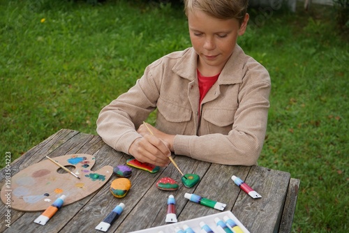 Boy turns humble stones into a rainbow harvest painting tiny avocado, carrot, eggplant with care.