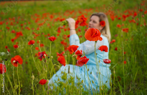 Woman poppies field. Happy woman is resting in the rays of the sun sitting in the poppy field.