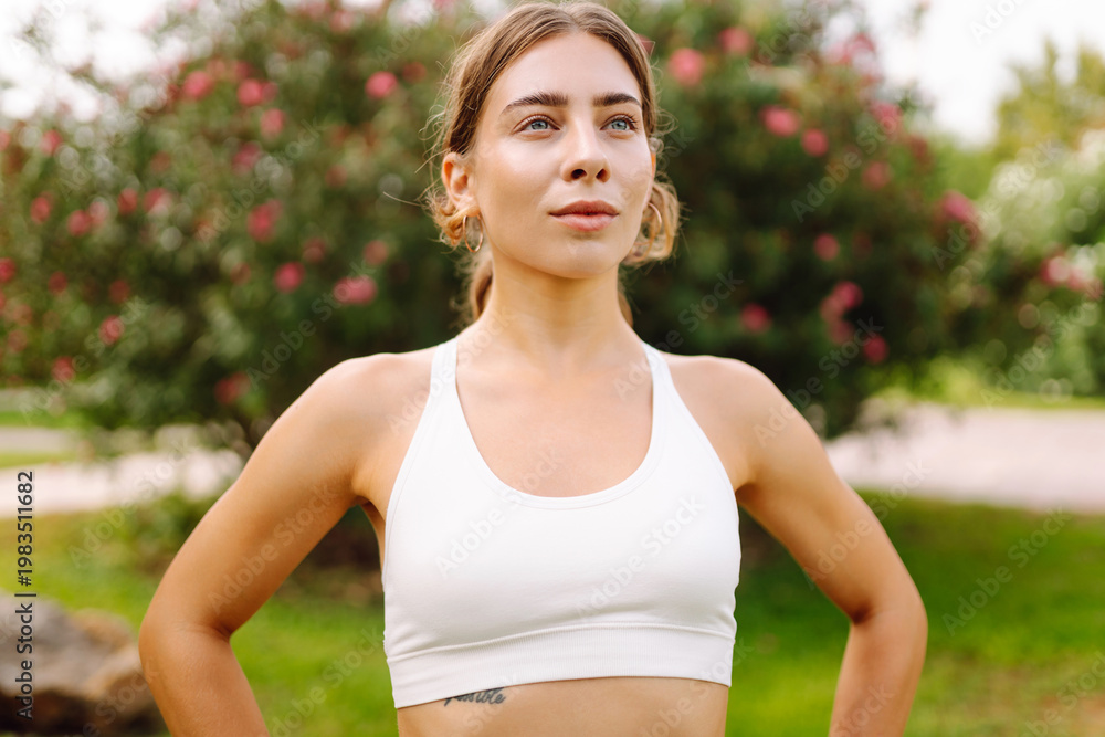 Fototapeta premium A woman in athletic clothes stretches on a yoga mat in a green park meadow. An athletic woman is working out outdoors. The concept of fitness, health, and enjoyment.