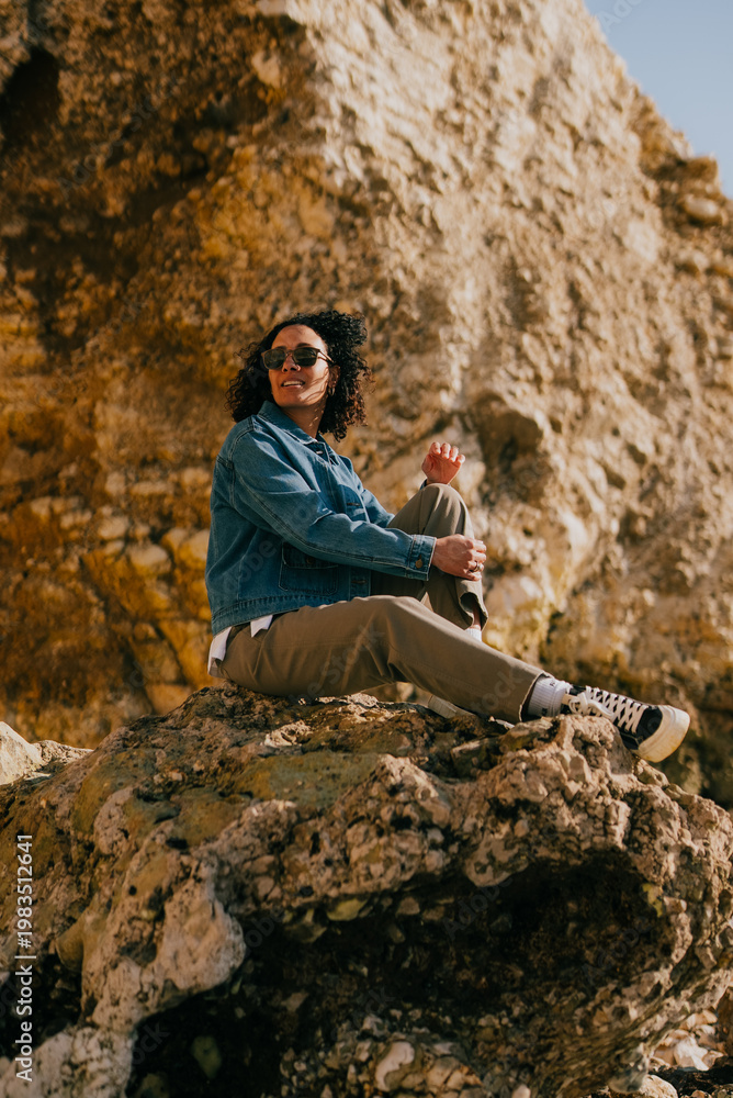 Naklejka premium Woman smiles warmly, seated on rocky cliffside