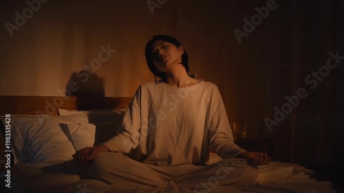 Young person meditating on bed in dimly lit cozy bedroom at night