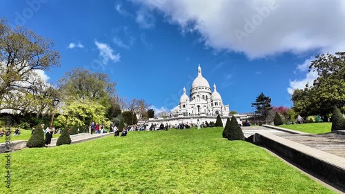 Low angle static shot of white clouds moving across a vibrant blue sky over the domes of the Sacré-Cœur Basilica.